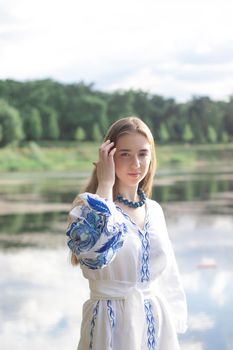 Portrait of young Ukrainian woman dressed in blue national traditional embroidered shirt in park outdoor.