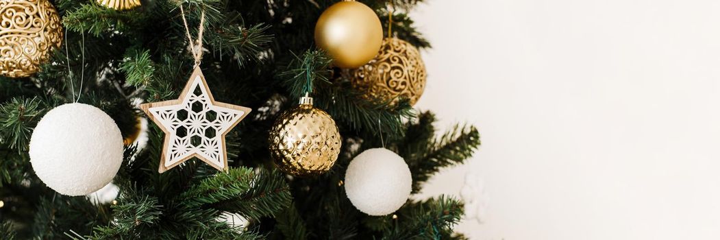 Gold and white Christmas ball on a Christmas tree in a light interior against the background of burning garlands of lights. Decorating Christmas tree on bright background. Web banner.