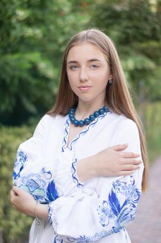 Portrait of young Ukrainian woman dressed in blue national traditional embroidered shirt in park outdoor.