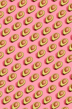 Food design. Top view of colorful fruit pattern of fresh cutted avocado halves with pits inside on coral pink pastel background. Mock up, flat lay style.