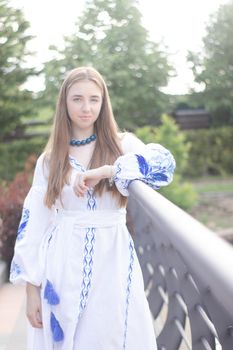 Portrait of young Ukrainian woman dressed in blue national traditional embroidered shirt in park outdoor.