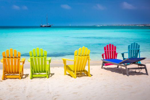 Colorful adirondack chairs on idyllic palm beach in Aruba with ship, Caribbean sea