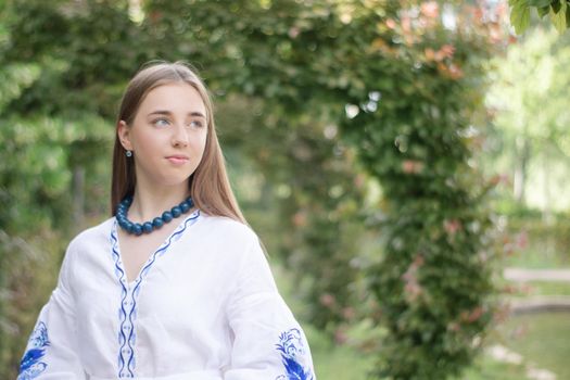 Portrait of young Ukrainian woman dressed in blue national traditional embroidered shirt in park outdoor.