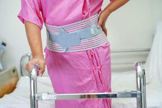 Asian senior pain back wearing elastic support belt with walker.