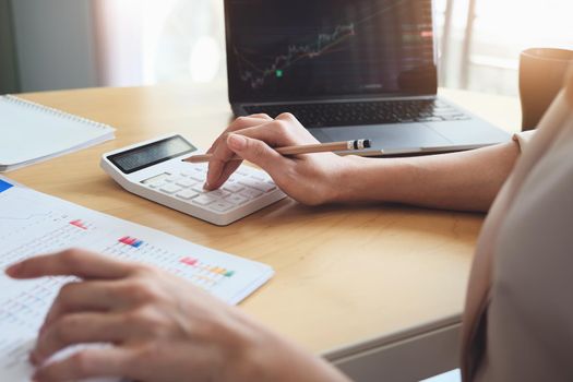 Business woman using calculator and computer to trade charts to find buy and sell points for her port.