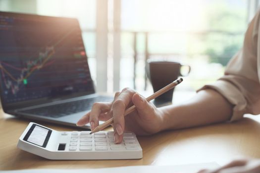 Business woman using calculator and computer to trade charts to find buy and sell points for her port.