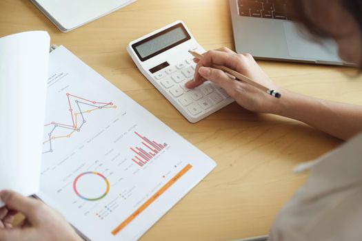 Business woman using calculator to review balance sheet annual using document and laptop computer to calculating budget. audit and Check integrity before investment concept.