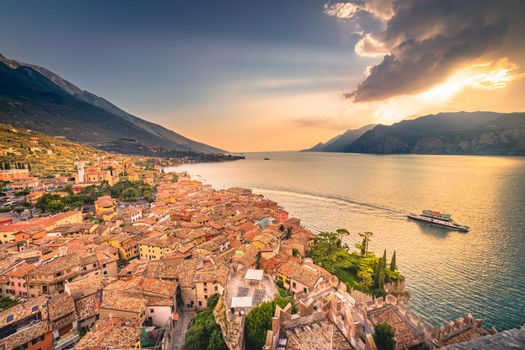 Malcesine roofs and fortress with boat cruise, Garda Lake and mountains, Italy.