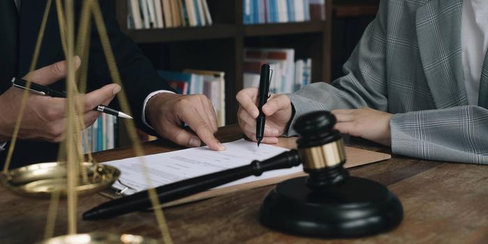 Business woman and lawyers discussing contract papers with brass scale on wooden desk in office. Law, legal services, advice, Justice concept.