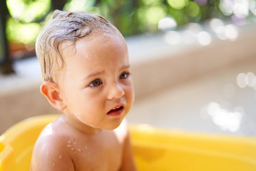 Little girl whimpers in a bowl of water. High quality photo