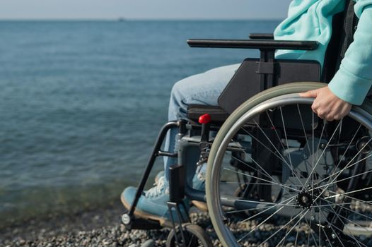 Caucasian woman in a wheelchair on the seashore. Close-up of female hands