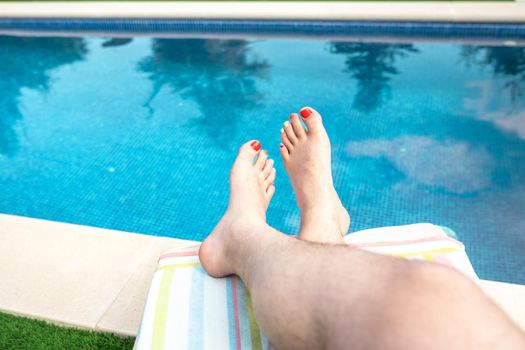 Close-up of the bare feet of a man relaxing on a sun lounger by a swimming pool. barefoot man with his nails painted in LGTBIQ colours. concept of travel and leisure. natural sunlight, outside, garden with swimming pool.
