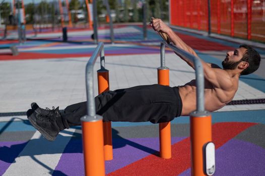 Shirtless man doing horizontal balance on parallel bars at sports ground