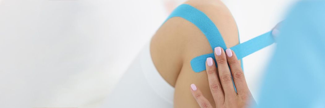 Close-up of physiotherapist put kinesiology blue tape on patient knee. Rehabilitation after injury or accident. Physical therapy, recovery, health concept