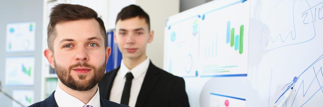 Portrait of smart people demonstrate some graphics and charts on white board. Attractive manager in classy suit and striped tie. Report, conference concept