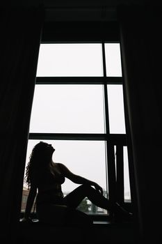 Gorgeous woman wearing black lingerie indoors. Portrait of a beautiful dreamy girl in a black underwear by the window. Black and white photo