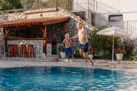 Excited boy in googles jumping in water from shoulders of his father standing in swimming pool