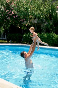 Dad throws a small child in the air over the water in the pool. High quality photo