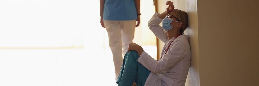 Low angle of female surgeon exhale after long operation sitting in clinic corridor on floor. Deserved rest after hard operation. Health, save life concept