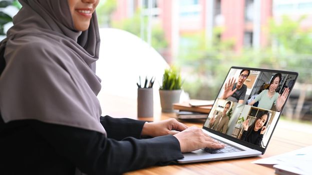 Smiling Muslim woman in hijab communicating by video conference on laptop computer.