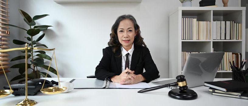 Experienced mature female lawyer sitting in her personal office and looking confidently to camera.