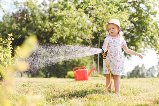 Adorable little girl playing with a garden hose on hot sunny summer day