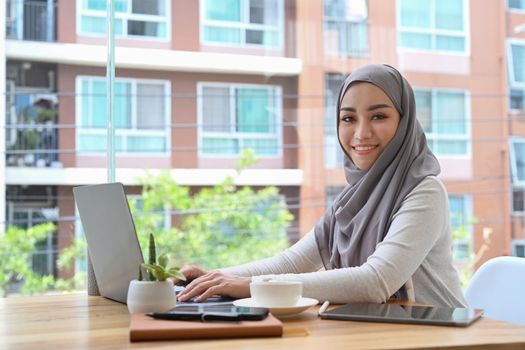 Elegant Muslim woman wearing hijab using computer laptop in her personal office.