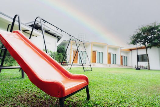 Orange slide in the playground. Playground equipment for children to play. Plastic slide at outdoor playground with green grass ground. Outdoor kids toy at park. Outdoor play equipment. Public space.