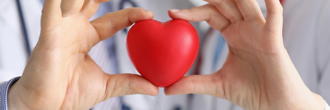 Close-up of medical workers colleagues together hold plastic red heart. Save life through donation or charity. Medicine, cardiology, healthcare concept