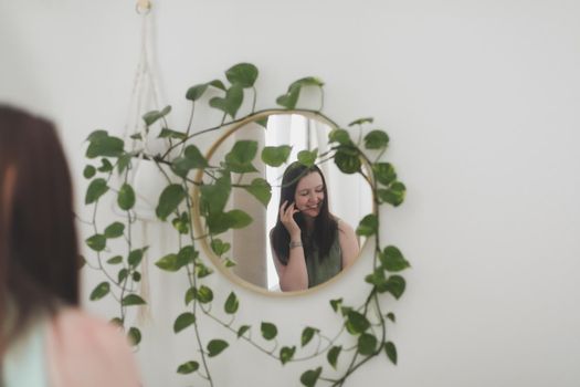 Young woman in apron as housewife or gardener takes care of green plant, watering flower pots in cozy room. gardening and hobby