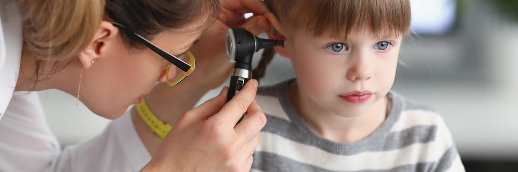 Portrait of little girl sit calm while family doctor examine ears with special equipment. Girl not afraid of doctors and clinic atmosphere. Health concept