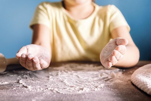 unrecognizable child with floured hands on the kitchen table that is full of flour, concept of healthy food at home