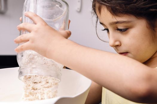 little girl pouring flour into a bowl to make homemade bread, concept of healthy food at home