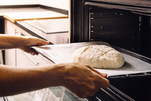 hands of an unrecognizable person putting a rustic bread dough in the oven, concept of healthy food at home