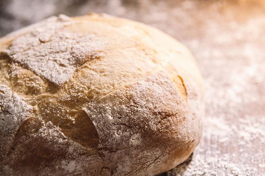 close-up of a freshly baked rustic bread illuminated by the morning sun on a wooden table full of flour, concept of healthy food at home