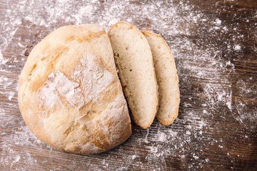 top view of a loaf of rustic bread cut on a wooden table full of flour, concept of healthy food at home