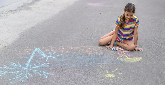 The child draws with chalk on the pavement. Selective focus. Kid.