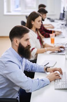 People working in modern IT office. Group of young programmers and software developers sitting at desks working on computers. Team at work.