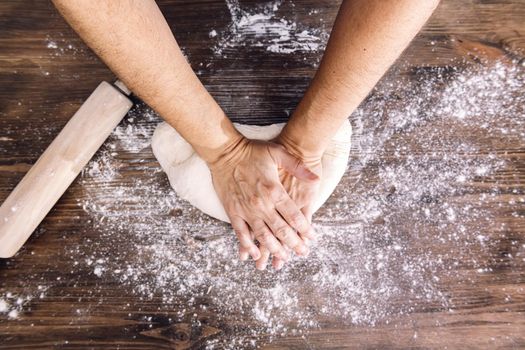 hands of an unrecognizable person kneading bread dough on a wooden table, concept of healthy food at home