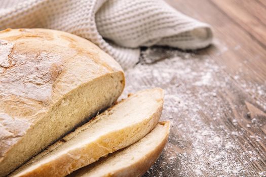 close up of a loaf of rustic bread cut into slices on a wooden table full of flour, concept of healthy food at home