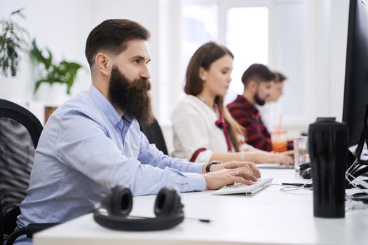 People working in modern IT office. Group of young programmers and software developers sitting at desks working on computers. Team at work.