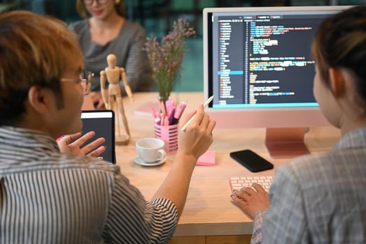 Asian software developers team brainstorming and programming on desktop computer in modern office.