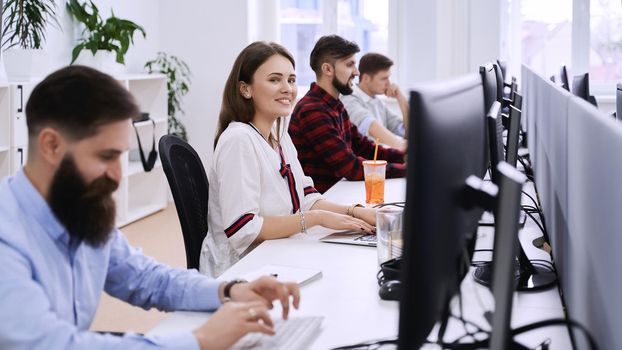 People working in modern IT office. Group of young programmers and software developers sitting at desks working on computers. Team at work.