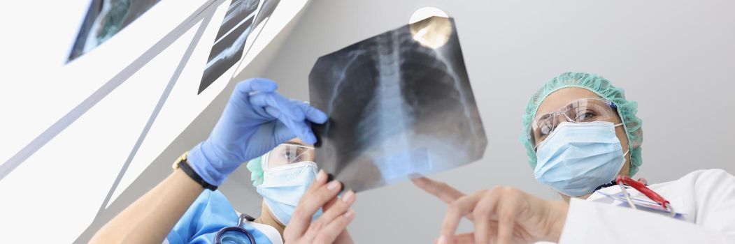Low angle of doctors in medical gowns examine x ray of patient lungs in clinic. Clinic workers got result and analyze medical history. Health, help concept