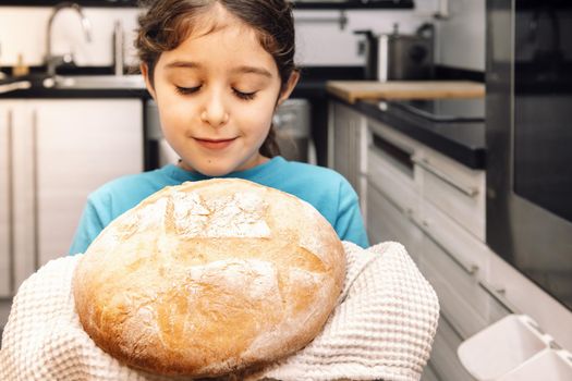 little girl smelling a loaf of freshly baked rustic bread in the kitchen, concept of healthy food at home