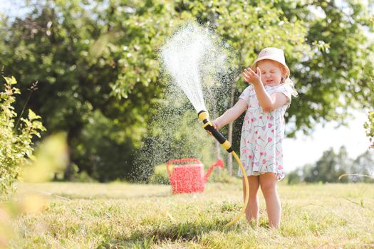 Adorable little girl playing with a garden hose on hot sunny summer day