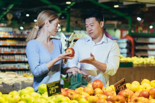 Arguing in supermarket, multiracial couple, asian husband and wife, choosing fruits and food, can't agree on choosing apples