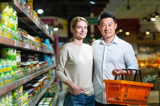 Happy married couple Asian man and woman looking at camera and smiling in grocery supermarket, choosing goods