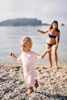 Little girl walks barefoot on a pebble beach. High quality photo