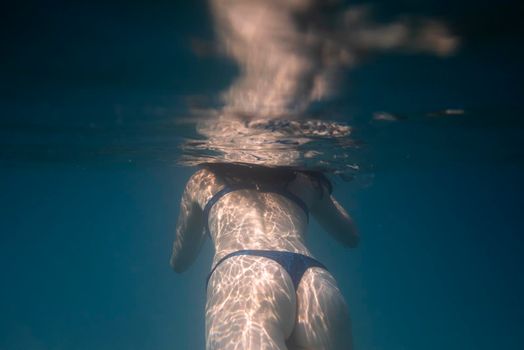 Woman swimming underwater in the ocean in clear blue water.